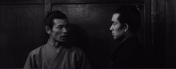 Movie still from “Red Beard” (1965), directed by Akira Kurosawa – Two asian men standing next to each other in front of a wooden wall; Close Up shot, Over the shoulder angle