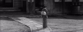 Movie still from “Red Beard” (1965), directed by Akira Kurosawa – A woman in a kimono is standing on the sidewalk; Wide shot, High angle