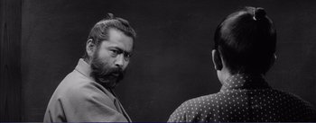 Movie still from “Red Beard” (1965), directed by Akira Kurosawa – A man with long hair and a beard standing next to another man with long hair; Close Up shot, Over the shoulder angle