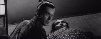 Movie still from “Red Beard” (1965), directed by Akira Kurosawa – A man standing next to a woman in a black and white photo; Close Up shot, Low angle