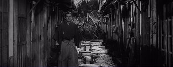 Movie still from “Red Beard” (1965), directed by Akira Kurosawa – A man standing in front of some buildings; Wide shot, High angle
