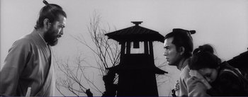 Movie still from “Red Beard” (1965), directed by Akira Kurosawa – A black - and - white photo of two men looking at each other in front of a building; Medium shot, Low angle