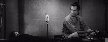 Movie still from “Red Beard” (1965), directed by Akira Kurosawa – A black and white photo of a man sitting next to a candle; Medium shot, High angle