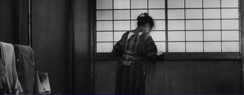 Movie still from “Red Beard” (1965), directed by Akira Kurosawa – A woman standing in front of a window with her hands on the wall; Medium shot, Low angle