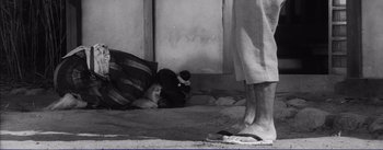 Movie still from “Red Beard” (1965), directed by Akira Kurosawa – A black and white photo of a person standing next to a sleeping cat; Wide shot, High angle