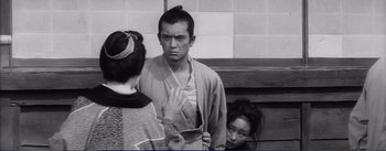 Movie still from “Red Beard” (1965), directed by Akira Kurosawa – A man and two women are standing in front of a brick wall; Medium shot, Over the shoulder angle