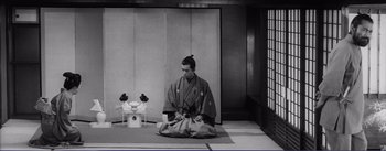Movie still from “Red Beard” (1965), directed by Akira Kurosawa – A man sitting on the ground in front of a building; Wide shot, Low angle