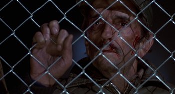 Movie still from “Red Dawn” (1984), directed by John Milius – A man with blood on his face looking through a chain link fence; Close Up shot, Low angle