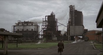 Movie still from “Red Desert” (1964), directed by Michelangelo Antonioni – A man is standing on the side of the road in front of a factory; Extreme Wide shot, High angle