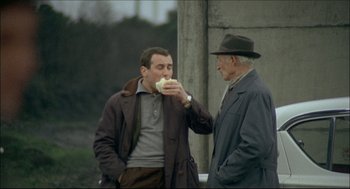 Movie still from “Red Desert” (1964), directed by Michelangelo Antonioni – Two men standing next to each other and one of them is eating a sandwich; Medium shot, High angle