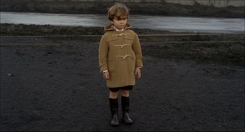 Movie still from “Red Desert” (1964), directed by Michelangelo Antonioni – A young boy wearing a brown coat and black boots; Wide shot, High angle