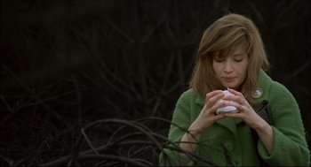 Movie still from “Red Desert” (1964), directed by Michelangelo Antonioni – A woman in a green sweater holding a white object in her hands; Medium shot, High angle
