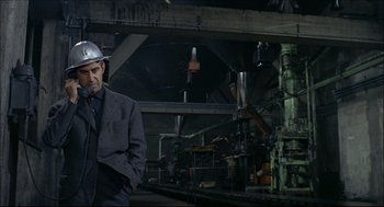 Movie still from “Red Desert” (1964), directed by Michelangelo Antonioni – A man wearing a hard hat in an industrial setting; Medium shot, Low angle