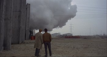 Movie still from “Red Desert” (1964), directed by Michelangelo Antonioni – Two men standing in front of a large cloud of smoke; Wide shot, Over the shoulder angle