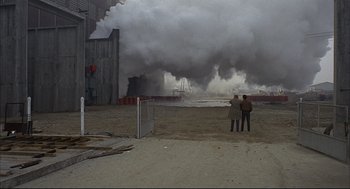 Movie still from “Red Desert” (1964), directed by Michelangelo Antonioni – Two people standing in front of a large cloud of smoke; Extreme Wide shot, High angle