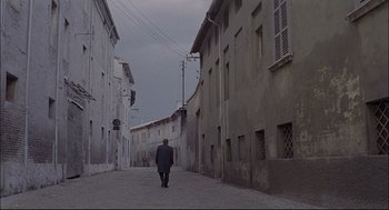 Movie still from “Red Desert” (1964), directed by Michelangelo Antonioni – A man walking down a street in a suit; Extreme Wide shot, High angle