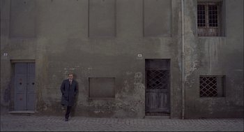 Movie still from “Red Desert” (1964), directed by Michelangelo Antonioni – A man standing in front of an old building; Wide shot, Low angle