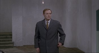 Movie still from “Red Desert” (1964), directed by Michelangelo Antonioni – A man wearing a suit and tie standing in a room; Medium shot, Low angle