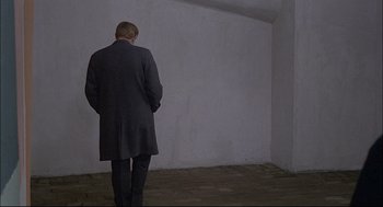 Movie still from “Red Desert” (1964), directed by Michelangelo Antonioni – A man standing in a room with his hands in his pockets; Wide shot, Over the shoulder angle