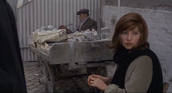 Movie still from “Red Desert” (1964), directed by Michelangelo Antonioni – A woman sitting in front of a cart with a man standing behind it; Medium shot, Over the shoulder angle