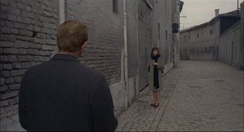 Movie still from “Red Desert” (1964), directed by Michelangelo Antonioni – A man and a woman standing on a brick sidewalk; Wide shot, Over the shoulder angle