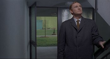Movie still from “Red Desert” (1964), directed by Michelangelo Antonioni – A man in a suit standing in front of an open door; Medium shot, Low angle