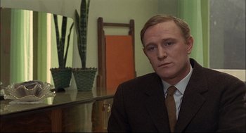 Movie still from “Red Desert” (1964), directed by Michelangelo Antonioni – A man wearing a suit and tie sitting in front of a mirror; Close Up shot, Over the shoulder angle