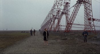 Movie still from “Red Desert” (1964), directed by Michelangelo Antonioni – A woman standing on a dirt road in front of a power line; Extreme Wide shot, Low angle