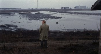 Movie still from “Red Desert” (1964), directed by Michelangelo Antonioni – A man standing in front of a body of water; Wide shot, High angle