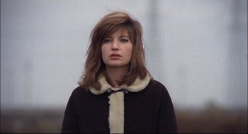 Movie still from “Red Desert” (1964), directed by Michelangelo Antonioni – A young woman with long brown hair wearing a black coat; Close Up shot, Low angle