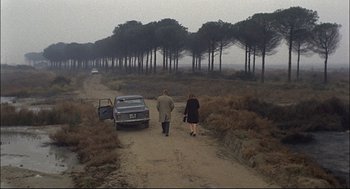 Movie still from “Red Desert” (1964), directed by Michelangelo Antonioni – A man and a woman walking down a dirt road; Wide shot, High angle