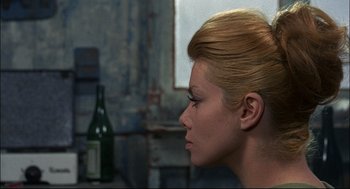 Movie still from “Red Desert” (1964), directed by Michelangelo Antonioni – A woman with a bottle of wine in the background; Close Up shot, Over the shoulder angle