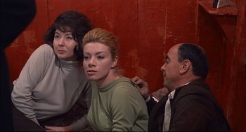 Movie still from “Red Desert” (1964), directed by Michelangelo Antonioni – A group of people sitting next to each other on a red wall; Medium shot, Over the shoulder angle