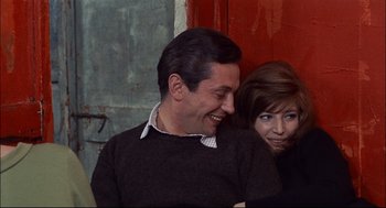 Movie still from “Red Desert” (1964), directed by Michelangelo Antonioni – A man and a woman are smiling for the camera; Medium shot, High angle