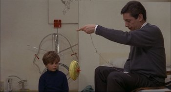 Movie still from “Red Desert” (1964), directed by Michelangelo Antonioni – A young boy sitting on the floor next to an older man; Medium shot, Over the shoulder angle