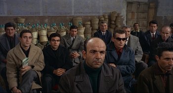 Movie still from “Red Desert” (1964), directed by Michelangelo Antonioni – A group of men sitting next to each other in a room; Medium shot, High angle