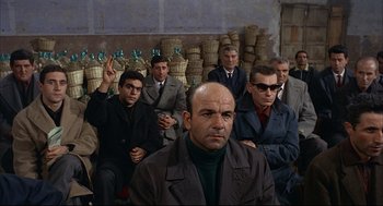 Movie still from “Red Desert” (1964), directed by Michelangelo Antonioni – A group of men sitting next to each other in a room; Wide shot, High angle