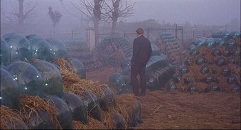 Movie still from “Red Desert” (1964), directed by Michelangelo Antonioni – A man in a suit standing in front of hay bales; Wide shot, High angle