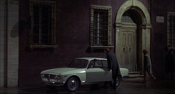 Movie still from “Red Desert” (1964), directed by Michelangelo Antonioni – A man is standing next to a white car; Wide shot, High angle