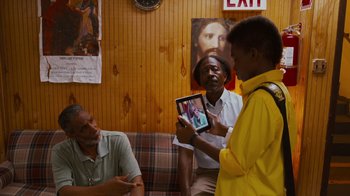 Movie still from “Red Hook Summer” (2012), directed by Spike Lee – A group of men standing around each other holding a tablet; Medium shot, Over the shoulder angle