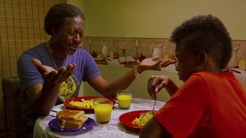 Movie still from “Red Hook Summer” (2012), directed by Spike Lee – Two people sitting at a table eating macaroni and cheese; Medium shot, Over the shoulder angle