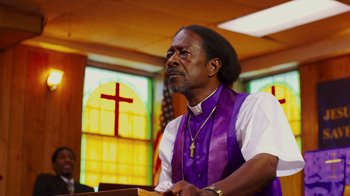 Movie still from “Red Hook Summer” (2012), directed by Spike Lee – A man wearing a purple vest is holding a bible; Medium shot, Low angle