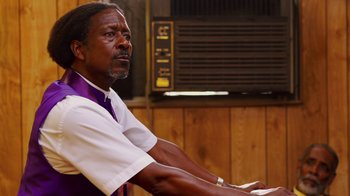 Movie still from “Red Hook Summer” (2012), directed by Spike Lee – A man sitting in front of a wooden wall; Close Up shot, Low angle