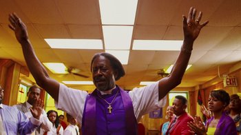Movie still from “Red Hook Summer” (2012), directed by Spike Lee – A man in a purple vest is raising his hands; Medium shot, Low angle