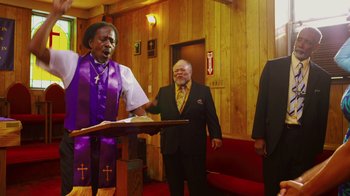 Movie still from “Red Hook Summer” (2012), directed by Spike Lee – Two men in suits and one man in a purple robe is standing at a podium; Medium shot, Low angle
