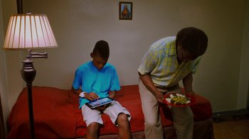 Movie still from “Red Hook Summer” (2012), directed by Spike Lee – A man and a boy sitting on a red couch; Medium shot, High angle