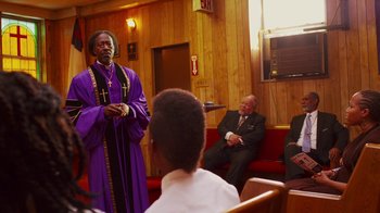 Movie still from “Red Hook Summer” (2012), directed by Spike Lee – A man in a priest's outfit standing in front of a group of people; Medium shot, Over the shoulder angle