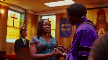 Movie still from “Red Hook Summer” (2012), directed by Spike Lee – A man and a woman holding hands in front of an american flag; Medium shot, Over the shoulder angle