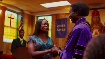 Movie still from “Red Hook Summer” (2012), directed by Spike Lee – A woman and a man shaking hands in front of stained glass windows; Medium shot, Low angle