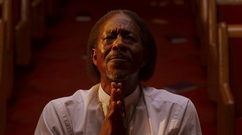 Movie still from “Red Hook Summer” (2012), directed by Spike Lee – An older black man is praying in front of a wall; Close Up shot, Low angle